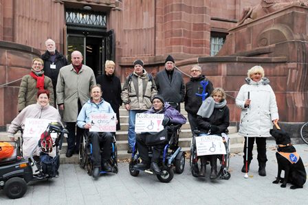 Das Foto zeigt Mitglieder und Unterstützer der AG Barrierefreiheit vor den elf unüberwindbaren Stufen am Löwenportal der Kunsthalle (Billingbau) bei der Protestaktion am 22.11.2013, darunter mehrere RollstuhlfahrerInnen und eine blinde Frau mit ihrem Blindenhund.