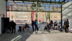 Foto mit einer Rollstuhlfahrer*innenschlange vor der Toilette am Platzhaus am alten Messplatz