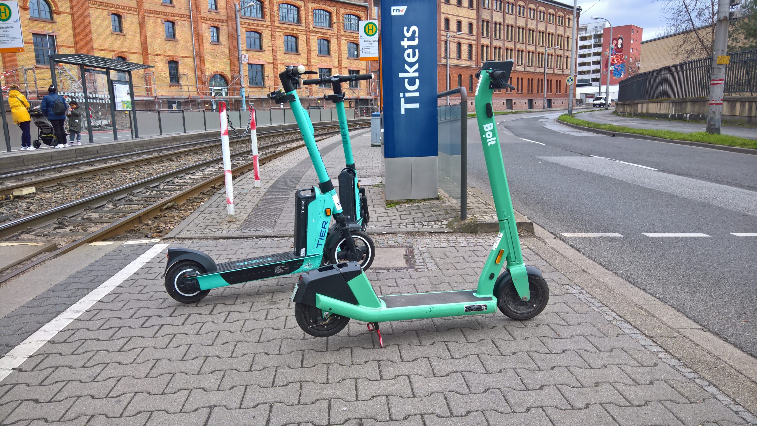 3 geparkte E-Tretroller stehen im Gehbereich einer Straßen- und Schienenquerung. Der Zugang zur rnv-Haltestelle ist blockiert. 